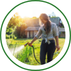 A woman uses a garden hose to water plants in her backyard.